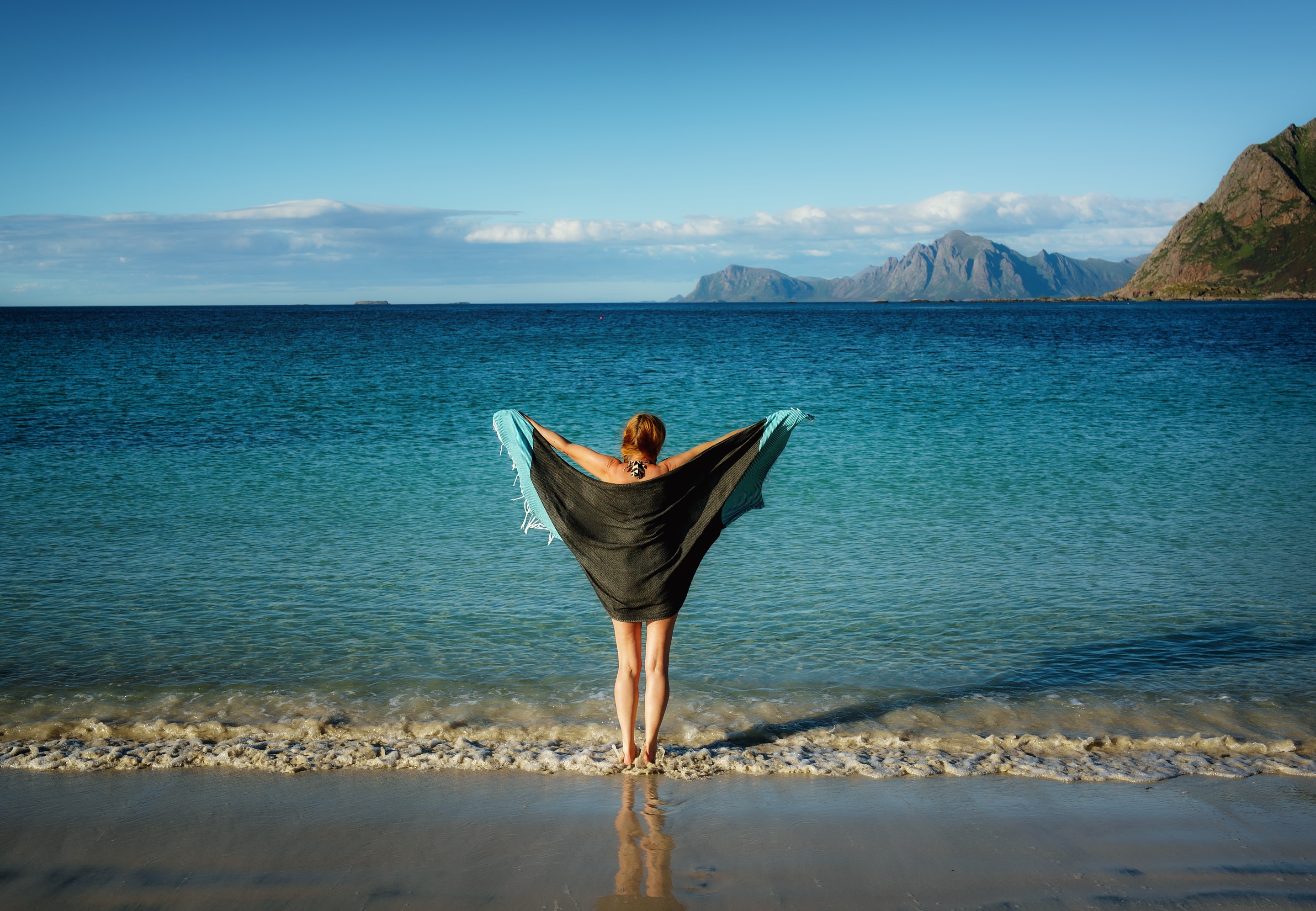 A woman holding a beach towel facing the beach