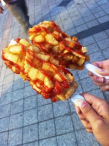 Two corn dogs on sticks topped with ketchup.