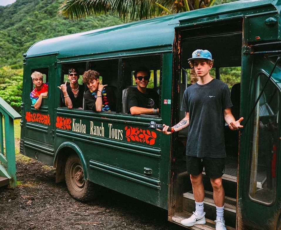 Five boys pose inside a bus with a sign on the side that says "Kualoa Ranch Tours".