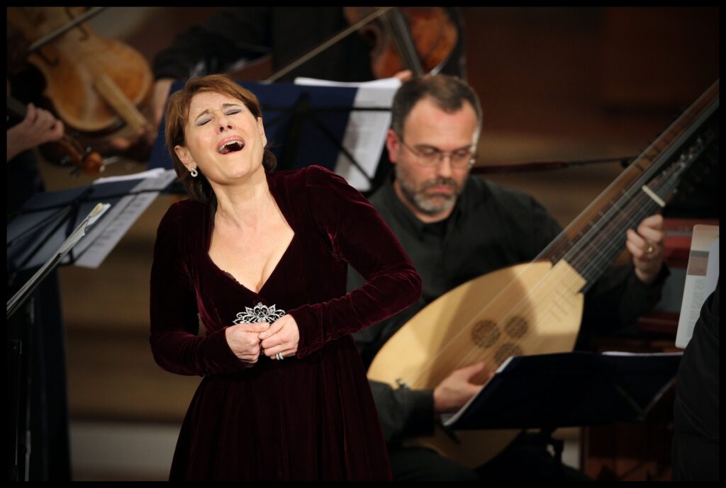 A woman in red velvet gown singing alongside an orchestra.