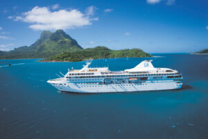 A white ship in the middle of the blue sea with green islets from behind.