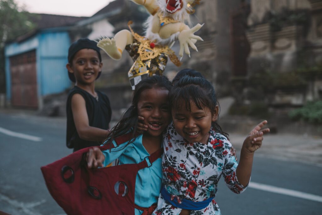 Two little girls happily hugging each other with a boy smiling from behind.