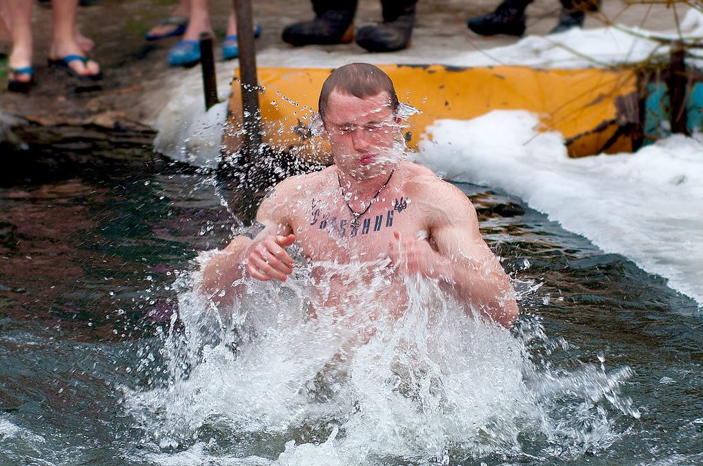 A guy splashes while swimming on an icy lake.