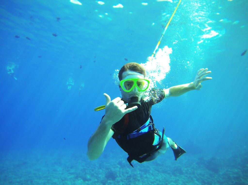 A guy poses while underwater, wearing googles and a breathing apparatus.