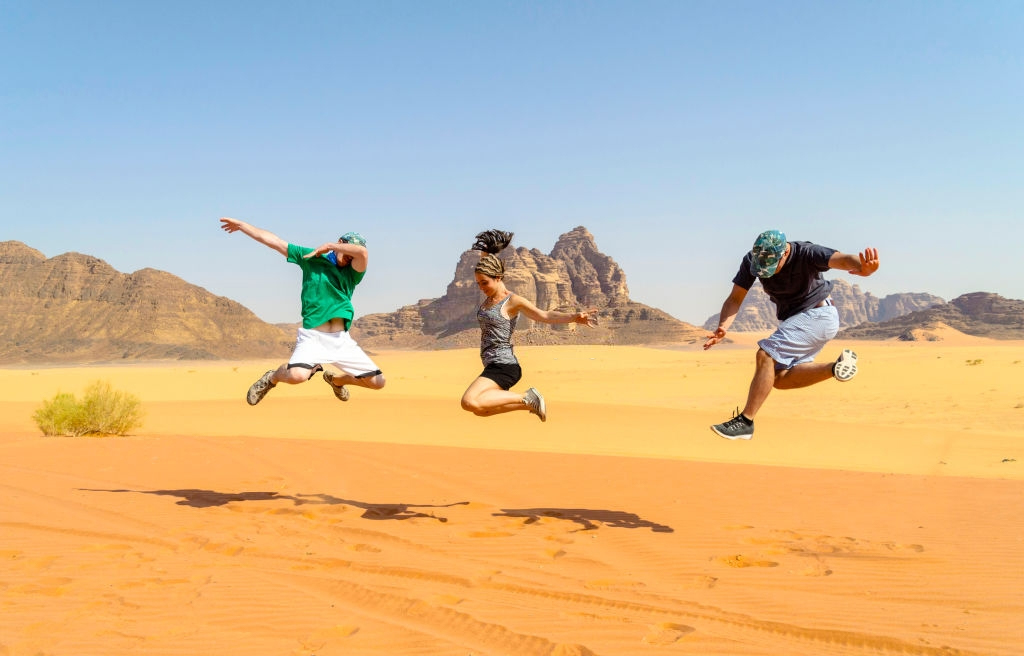 Male and female travelers doing jump posing for photo in Wadi Rum desert during the summer.