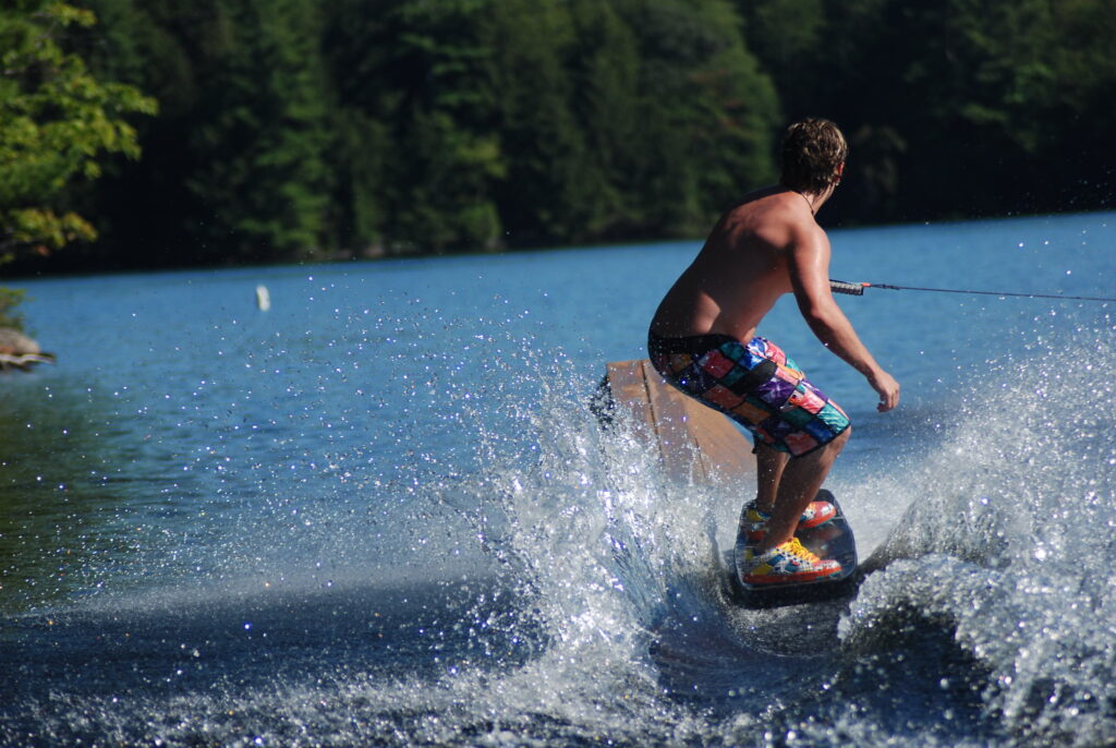 A guy on a wake-board preparing to pass a an inclined wooden platform.