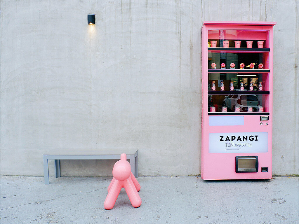 A pink vending machine beside a dog-shaped seat.