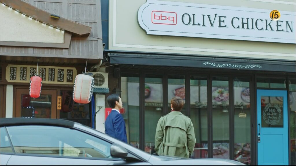 Two men outside a building with a sign that says BBQ Olive Chicken.