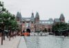 A park with a sign that says "I amsterdam" in front of a gabled building.