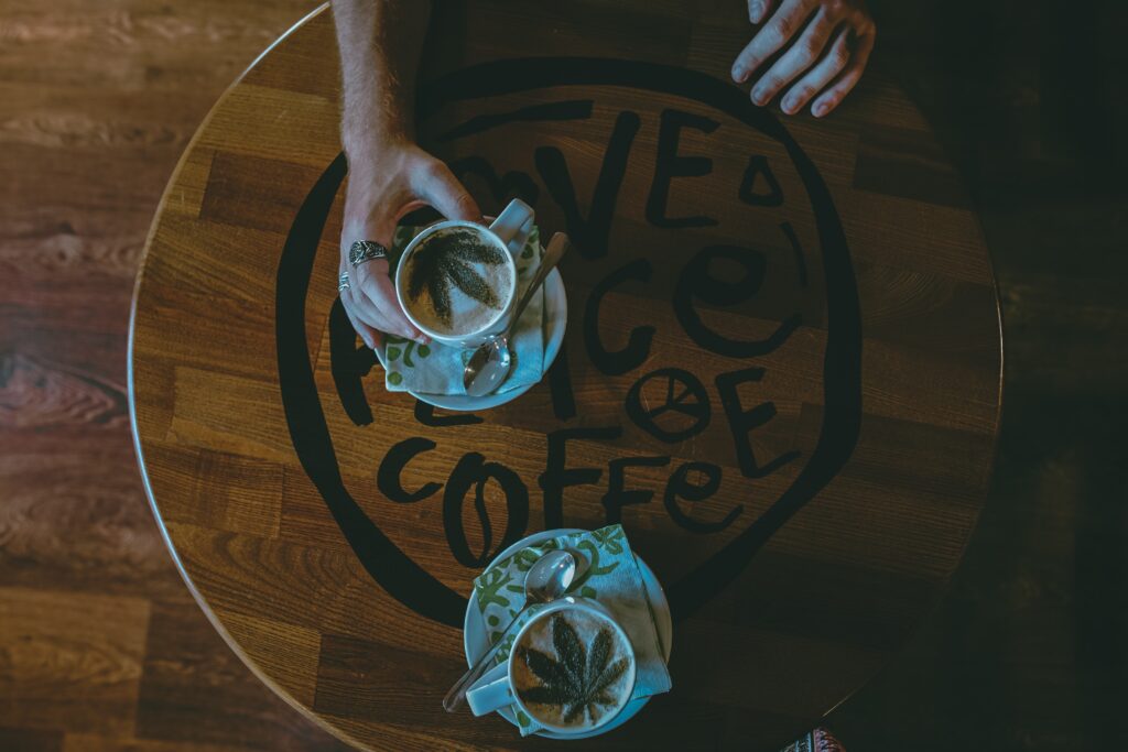 Two cups of latte with green powder on top shaped like cannabis.