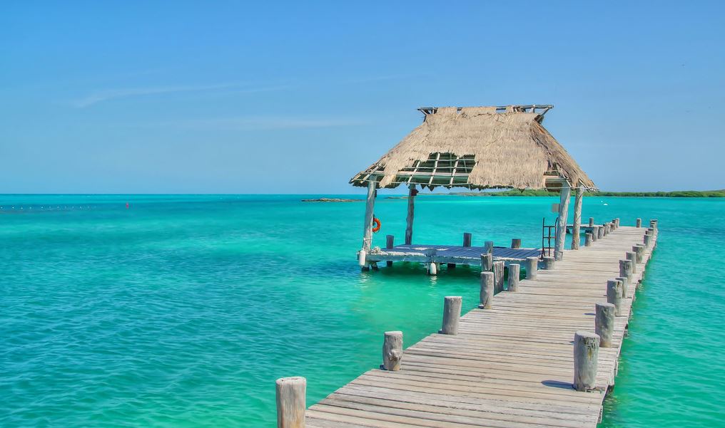 A wooden walkway leading to a hut on the middle of the sea.