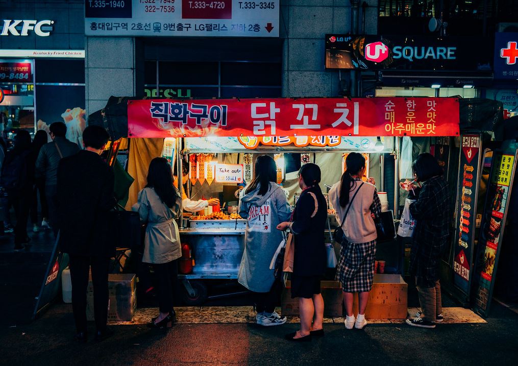 People in front of a food cart buying Korean street foods.