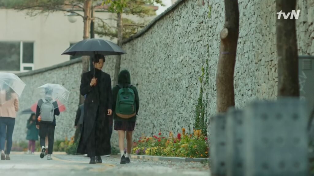 A girl in a hoodie jacket walks past a man carrying a black umbrella.