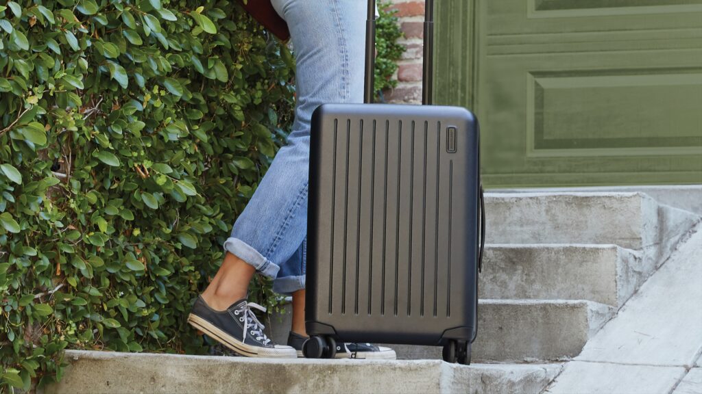 A person with a black luggage standing in cemented stairs.
