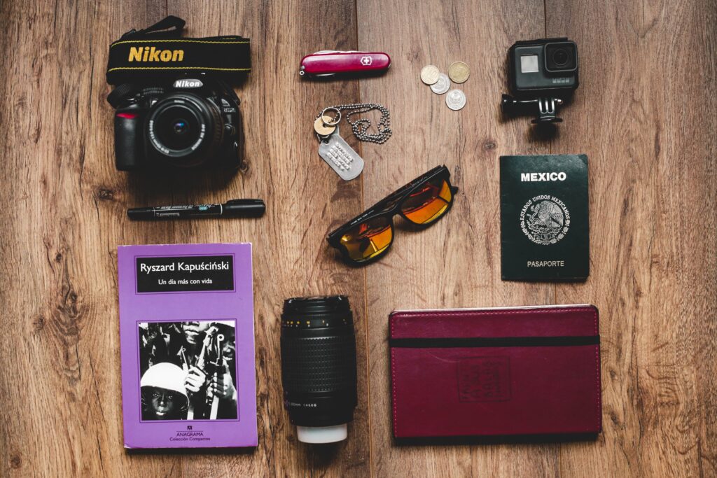 Flat lay photograph of travel essentials like passport, camera, planner, etc..